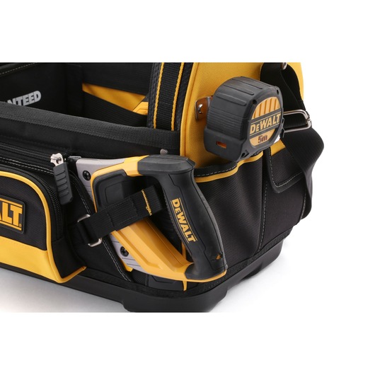 Close-up of a DEWALT tool bag featuring a staple gun and a tape measure attached to the bag. The bag is black and yellow with multiple compartments and durable construction.