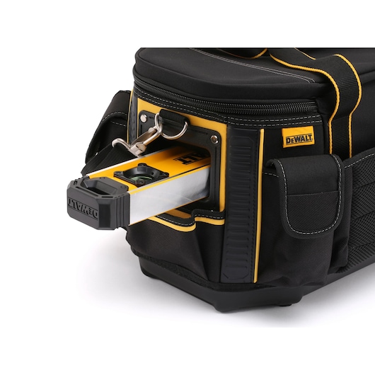 Close-up view of a black and yellow DEWALT tool bag with a level tool stored in a side pocket. The bag is made of durable fabric with multiple compartments and a zippered top.