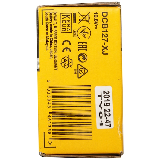 Close-up of a yellow DEWALT product box showing various certification symbols, barcode, and product code DCB127-XJ. The box displays information indicating the battery is made in China, Japan, South Korea, or Malaysia. The text also specifies 10.8V and includes a sticker with '2019 22-47 TY01'.
