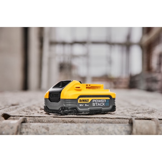 DEWALT POWERSTACK 18V 5Ah battery shown on a concrete surface in an industrial setting.