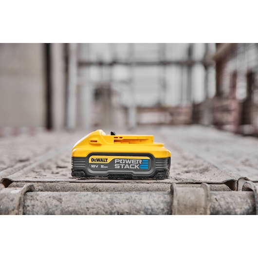 DEWALT POWERSTACK battery, 18V 5Ah, placed on a construction site, yellow and black design.