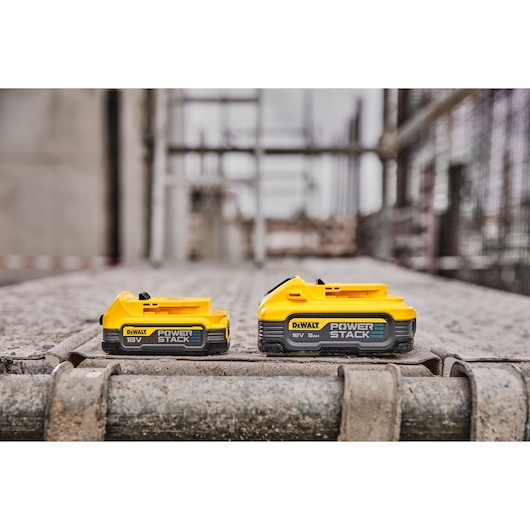 Two DEWALT POWERSTACK 18V batteries are shown on a construction site, placed side by side on a metal surface.