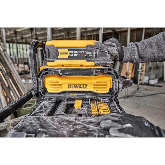 A DEWALT Power Shift battery pack being handled and installed on a DEWALT charging station at a construction site.