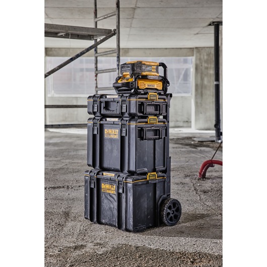 Stacked DEWALT ToughSystem toolboxes and organizers with wheels, standing on a construction site floor. The boxes are black with yellow accents and DEWALT branding.