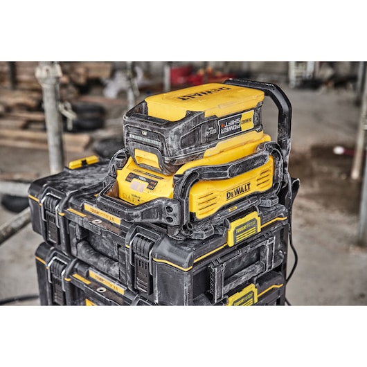 A yellow and black DEWALT battery charger and storage system, with dust marks, stacked on top of ToughSystem toolboxes at a construction site.