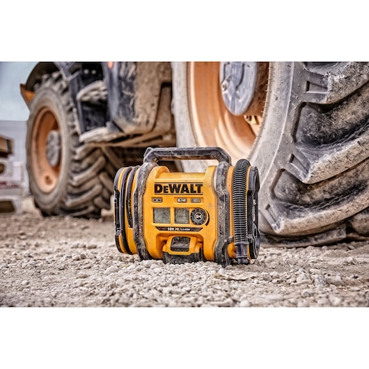 A DEWALT portable air compressor (model DCC018N) sits on a rough construction site ground next to a large vehicle tire.