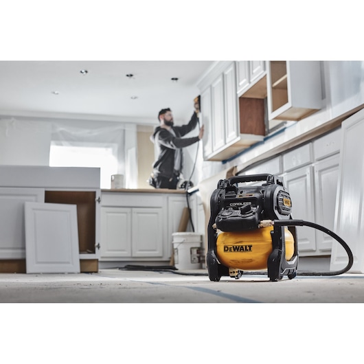 DEWALT cordless air compressor in a kitchen renovation setting with a worker using power tools.