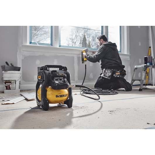 DEWALT cordless compressor in a room under renovation, worker using nail gun near window.