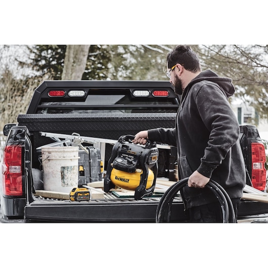 Person loading a DEWALT cordless compressor and tools onto a truck bed outdoors.