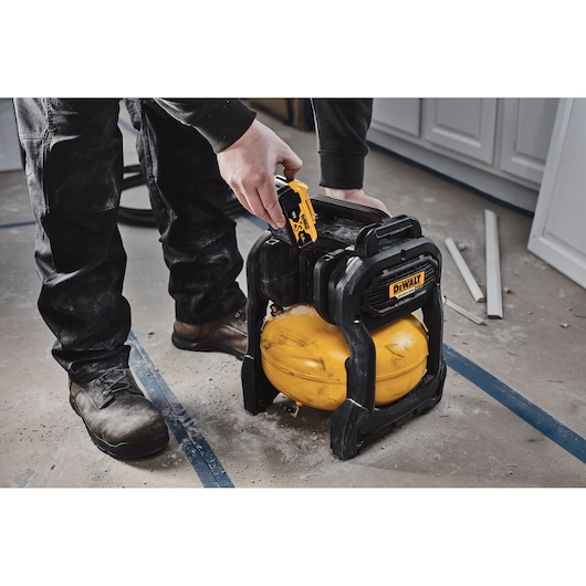Person using a DEWALT DCC1018N compact portable air compressor on a workshop floor.