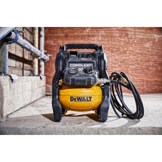 A DEWALT cordless air compressor with a yellow tank and black controls, positioned on a concrete floor with a hose attached. The compressor is branded with the DEWALT logo and is suitable for portable use.
