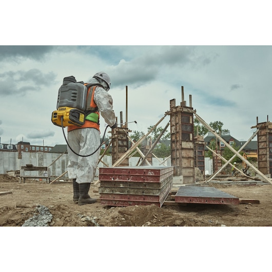 Worker with DEWALT DCCS1100N-XJ, DCCS1100N on construction site, wearing safety gear and spraying equipment.