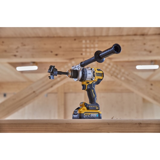 DEWALT cordless drill with auger bit and side handle on wooden beam in workshop setting.