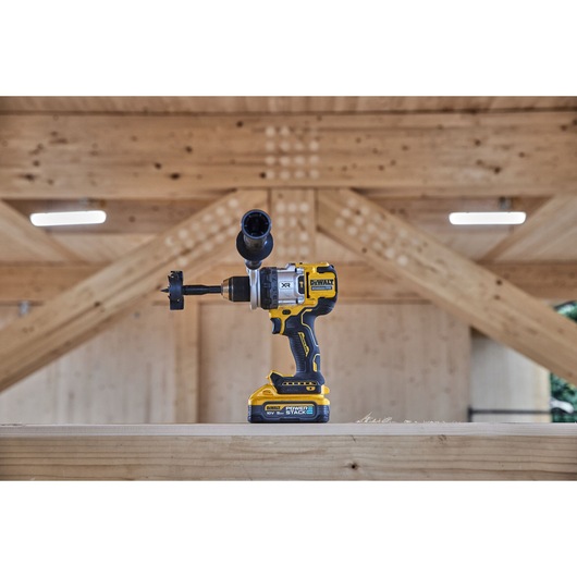 DEWALT cordless drill with bit attachment resting on a wooden beam in a workshop with wooden rafters.