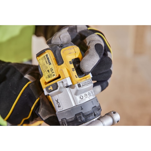 Gloved hand holds yellow DEWALT cordless drill, adjusting settings. The tool is used for professional construction work.