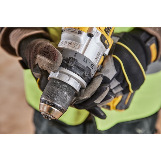 Gloved hands adjust a DEWALT cordless drill, focusing on the drill's chuck and settings dial.