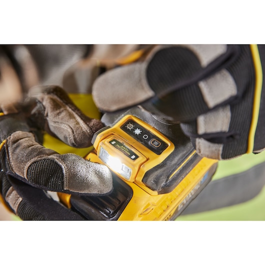 Gloved hands adjusting the control panel and LED light on a yellow DEWALT power tool.