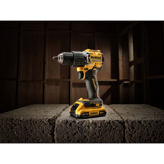 Yellow and black DEWALT cordless drill placed on concrete blocks in a dimly lit room.