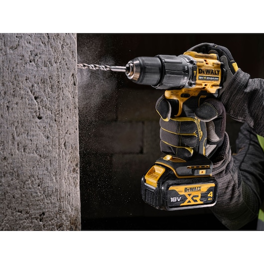 A person wearing protective gloves is operating a yellow and black DEWALT cordless drill, drilling into a concrete wall
