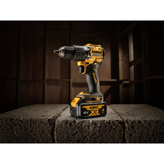 DEWALT cordless drill DCD100YM2T with 18V XR battery shown on concrete blocks in a workshop.