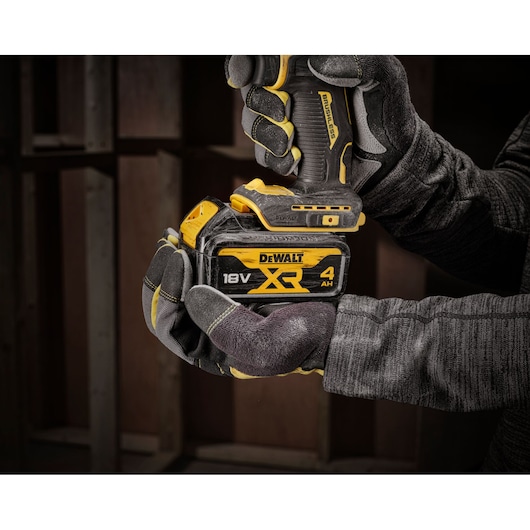 Gloved hands holding a DEWALT XR 18V cordless drill with a 4Ah battery in a dimly lit workshop.