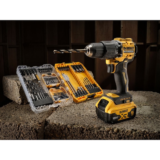DEWALT cordless drill with battery and two drill bit sets displayed on concrete blocks in a workshop setting.