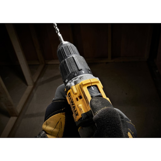 Gloved hand holding DEWALT cordless power drill with a bit, used in construction or woodworking.