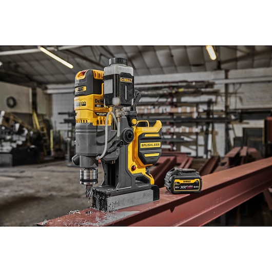 DEWALT cordless magnetic drill and battery placed on a steel beam in an industrial workshop setting.