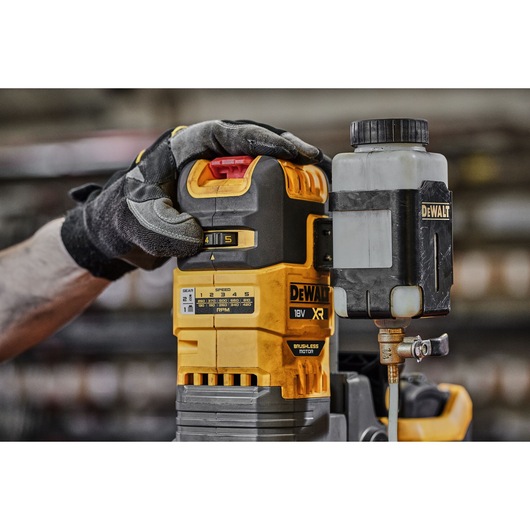 Gloved hand adjusts a DEWALT 18V XR brushless motor tool with attached container in a workshop setting.