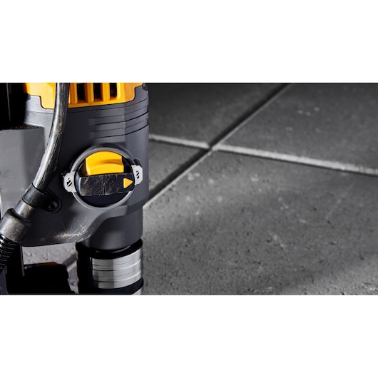 Close-up of a DEWALT tool with a yellow dial, placed on a tiled concrete surface.