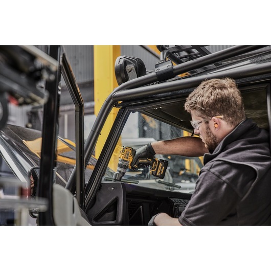 A person using a DEWALT cordless drill inside a vehicle, working on the dashboard area. The person’s face is blurred for privacy.