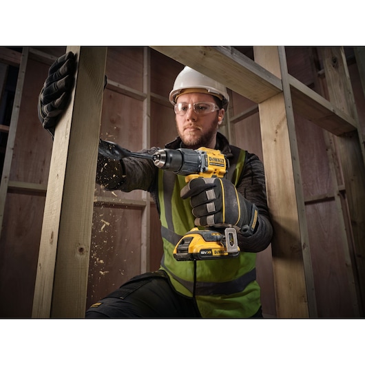 A person wearing safety gear uses a DEWALT cordless drill to drill into a wooden beam inside a construction site. Wood
