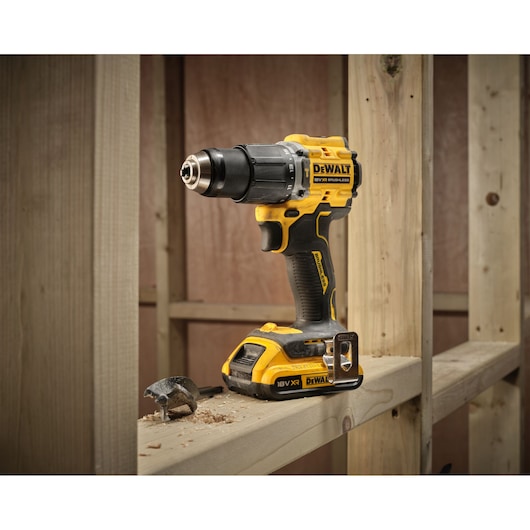 DEWALT cordless drill DCD799D2T with bit, placed on wooden beam at a construction site.