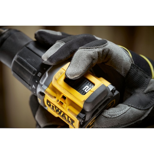 Gloved hand adjusts speed setting on a yellow DEWALT cordless drill.