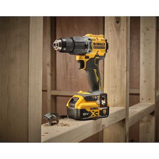 DEWALT 18V cordless drill on wooden beam with drill bit and wood shavings in construction setting.
