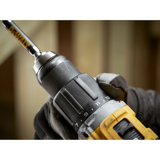 Close-up of a DEWALT cordless drill held by a gloved hand, showing the adjustable torque settings.