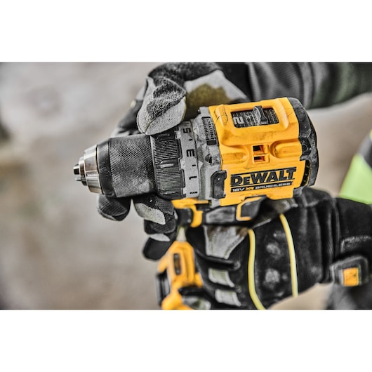 Gloved hand holding a yellow DEWALT cordless drill, close-up of the drill's body and settings.