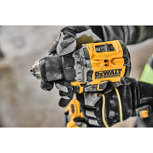 Close-up of a person wearing work gloves holding a DEWALT 18V XR brushless cordless drill, model DCD800P2T.