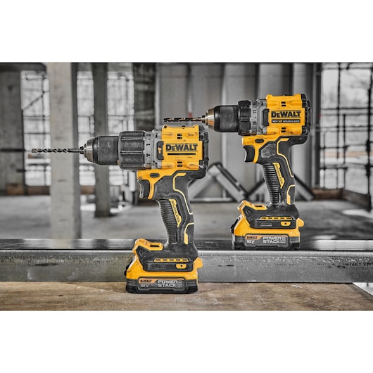 Two DEWALT cordless electric drills with yellow and black bodies and 18V POWERSTACK batteries are placed side by side on a metal surface inside a construction site.