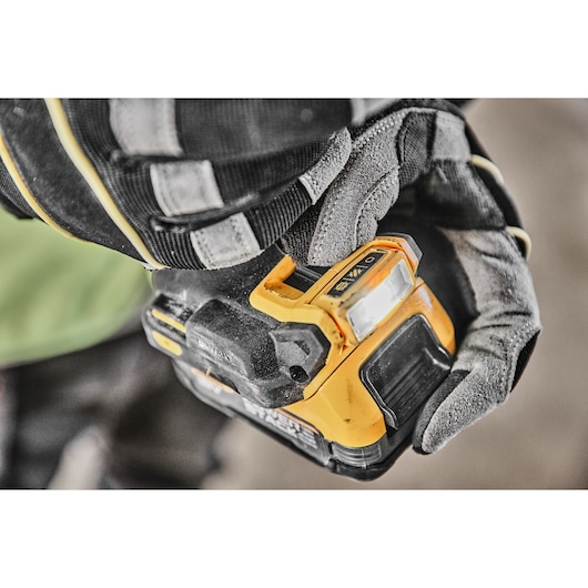 Close-up of a gloved hand holding a DEWALT cordless power drill with a visible LED work light and control switch.