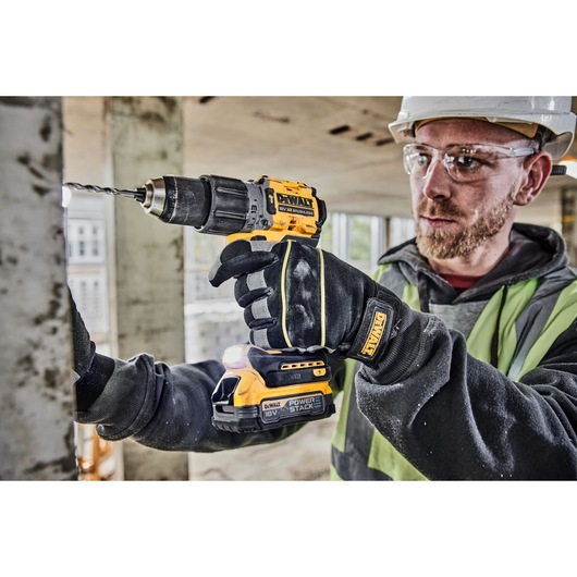 A worker in safety gear uses a DEWALT DCD805E2T 18V cordless drill with a POWERSTACK battery to drill into a metal surface