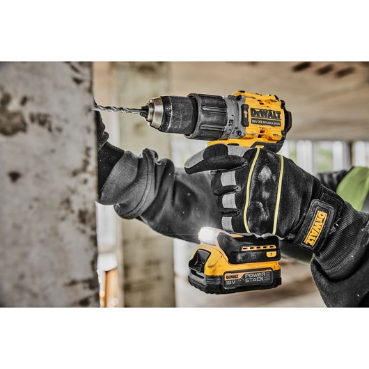 A close-up view of a person using a yellow and black DEWALT cordless drill to make a hole in a metal surface. The person is