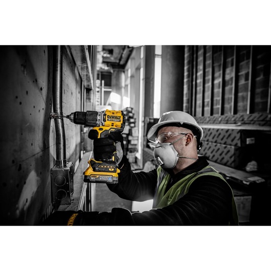 A person wearing a safety vest and hard hat uses a DEWALT DCD805E2T cordless drill to work on a metal pipe attached to a