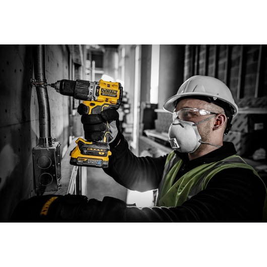 A person wearing a hard hat and safety vest is using a DEWALT DCD805E2T cordless power drill to work on a metal pipe