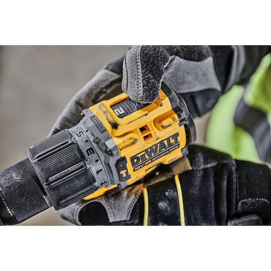 Gloved hand adjusts settings on a yellow DEWALT 18V XR brushless drill.