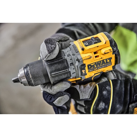 Gloved hand holding a yellow DEWALT DCD805H2T cordless drill with brushless motor close up.