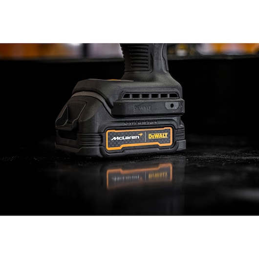 Close-up view of a DEWALT cordless power tool with a McLaren and DEWALT logo on the battery pack, placed on a reflective black surface.