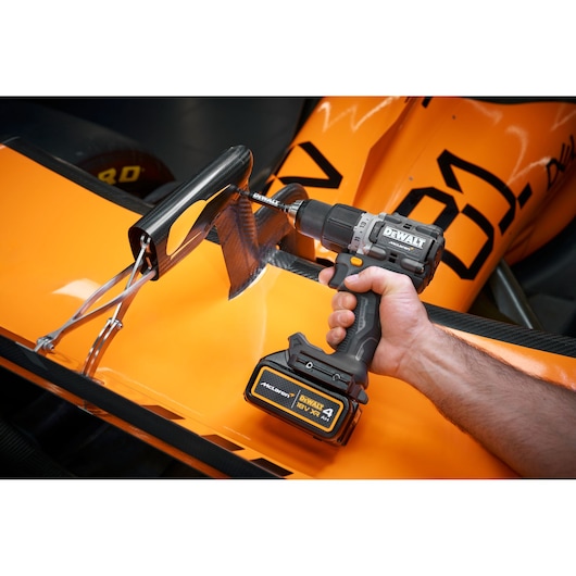 A person is using a DEWALT cordless drill, model DCD85MM1T, to work on the carbon fiber wing of an orange race car.