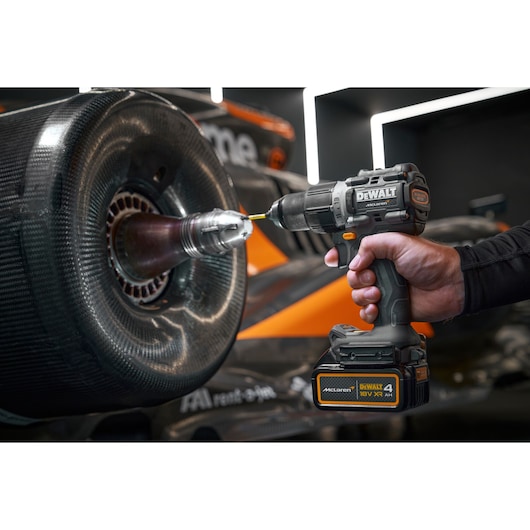 A close-up of a person using a DEWALT cordless drill, model DCD85MM1T, to work on the wheel hub of an orange and black race