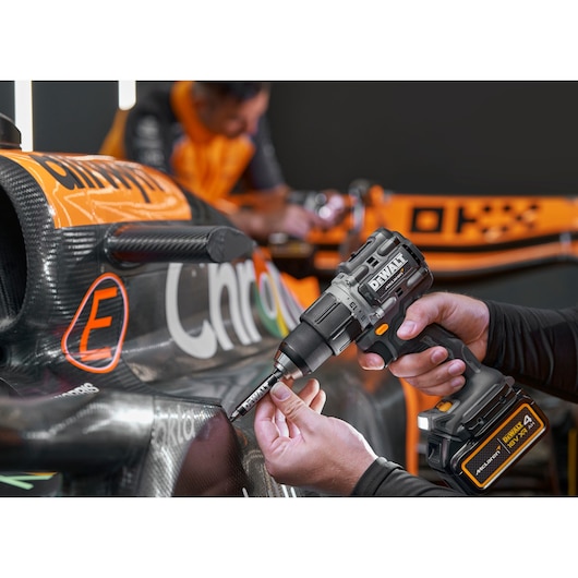 A person using a DEWALT cordless drill (model DCD85MM1T) to work on a carbon fiber race car, with another person in the